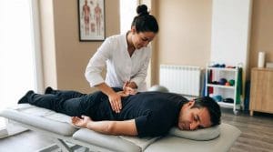 Fisioterapeuta aplicando terapia manual na região lombar de paciente deitado em maca em sala moderna.
