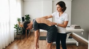 Fisioterapeuta orienta paciente jovem realizando o Teste de Adams para avaliar a coluna vertebral e detectar assimetrias.